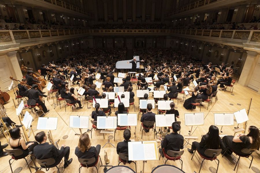 Blick auf Orchester, Dirigent und Publikum von hinter der Bühne