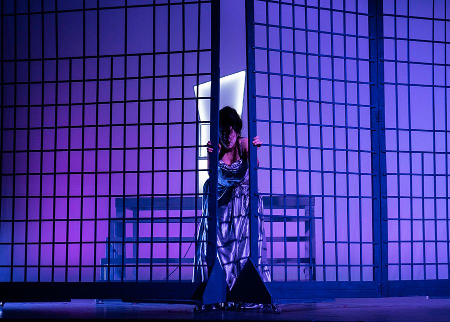 Gesangstudentin auf einer violett beleuchteten Bühne hinter einem Gittertor