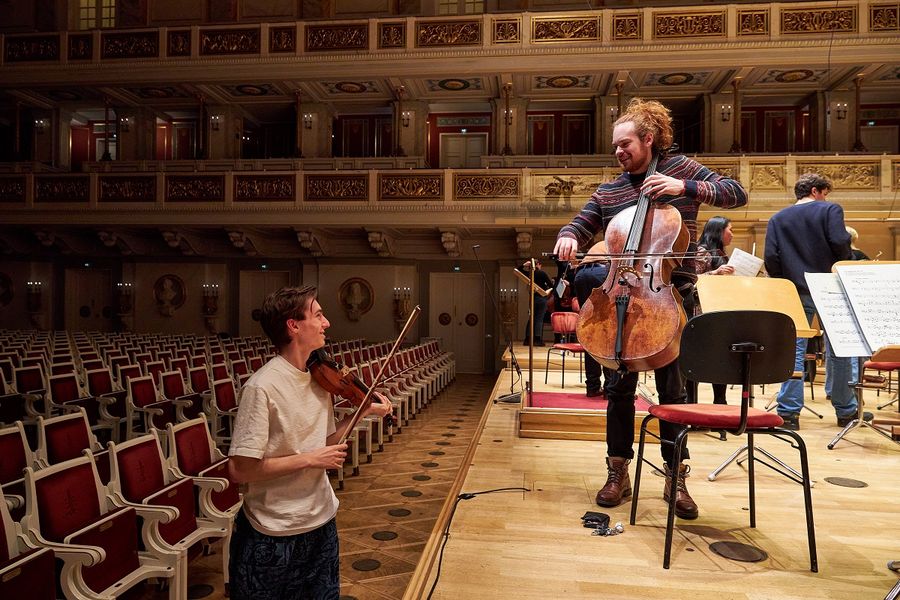 Ein Student steht auf der Bühne im Großen Saal des Konzerthaus Berlin und hält ein Cello in der Hand, vor der Bühne ein Student der eine Geige hält