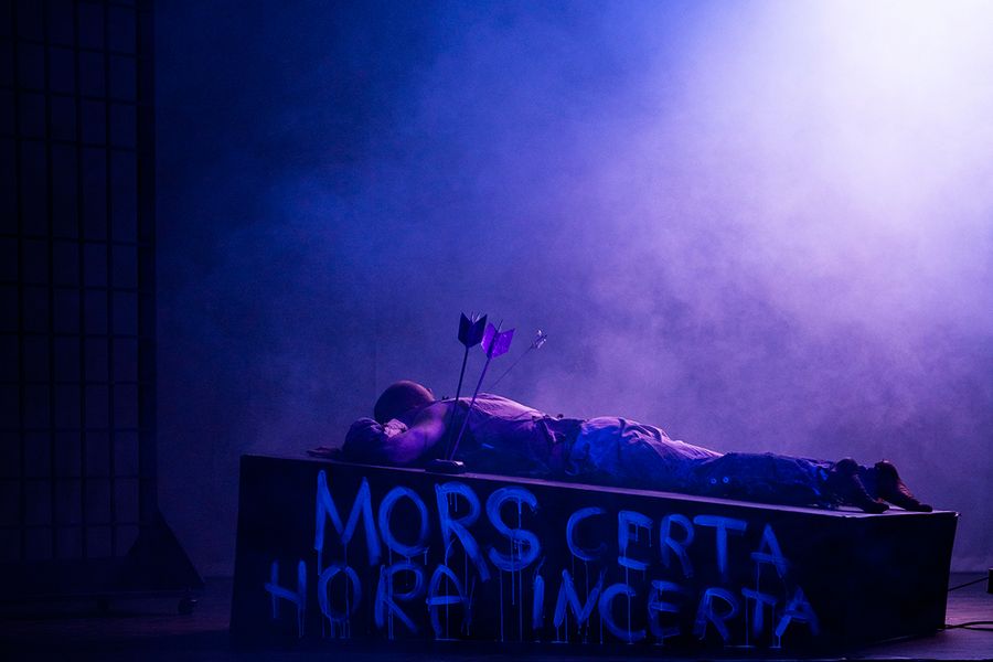 Gesangstudent mit Pfeil im Rücken liegt auf einer violett beleuchteten Bühne