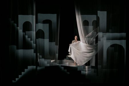 Gesangstudentin inmitten eines kontrastreich ausgeleuchteten Bühnenbilds mit Treppen und Torbögen
