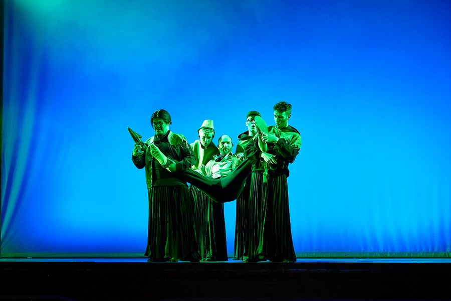 Vier singende Studierende in Kostümen auf einer Bühne tragen einen vierten in ihrer Mitte