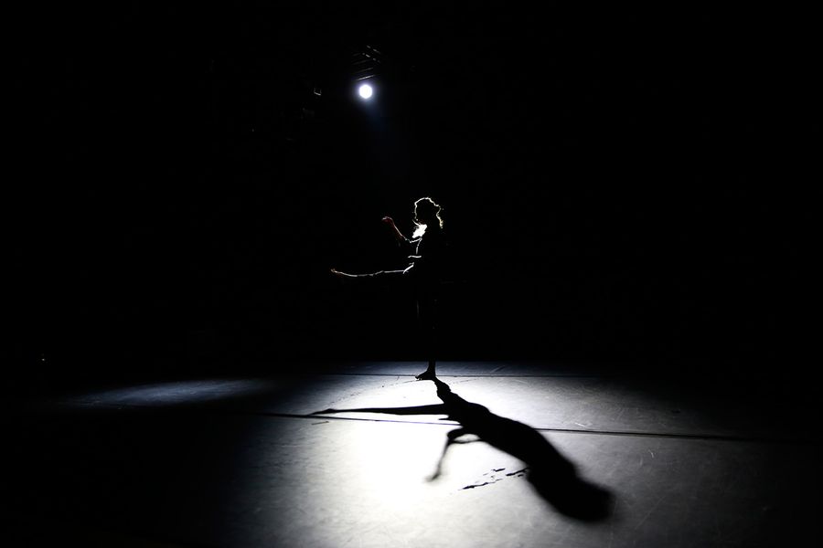 Silhouette eines tanzenden Menschen auf einer dunlen Bühne mit Lichtkegel 