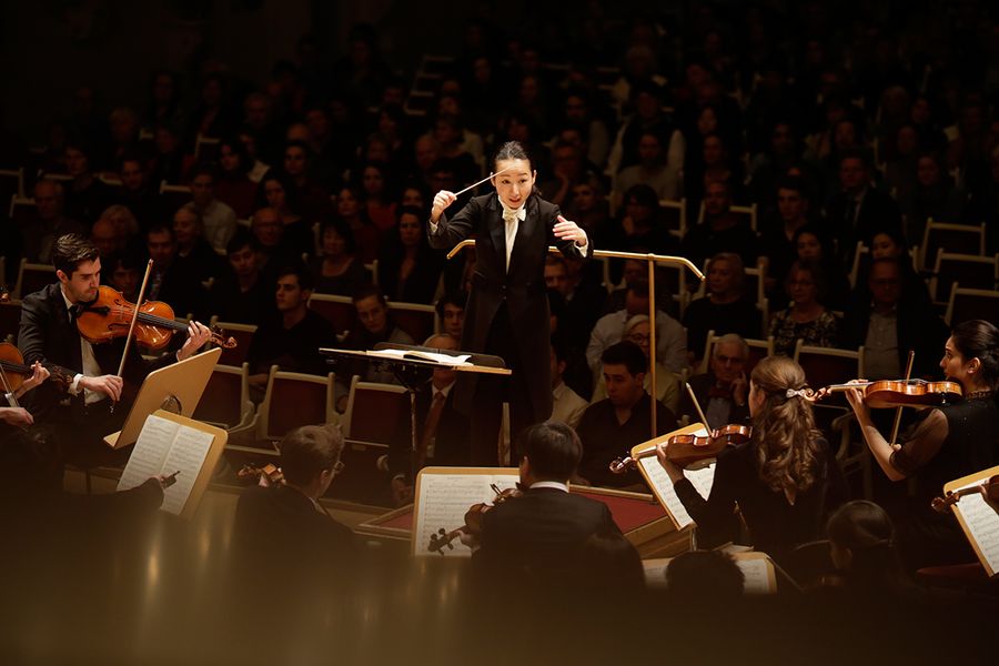 Studentin dirigiert ein Orchester in einem Saal mit Publikum