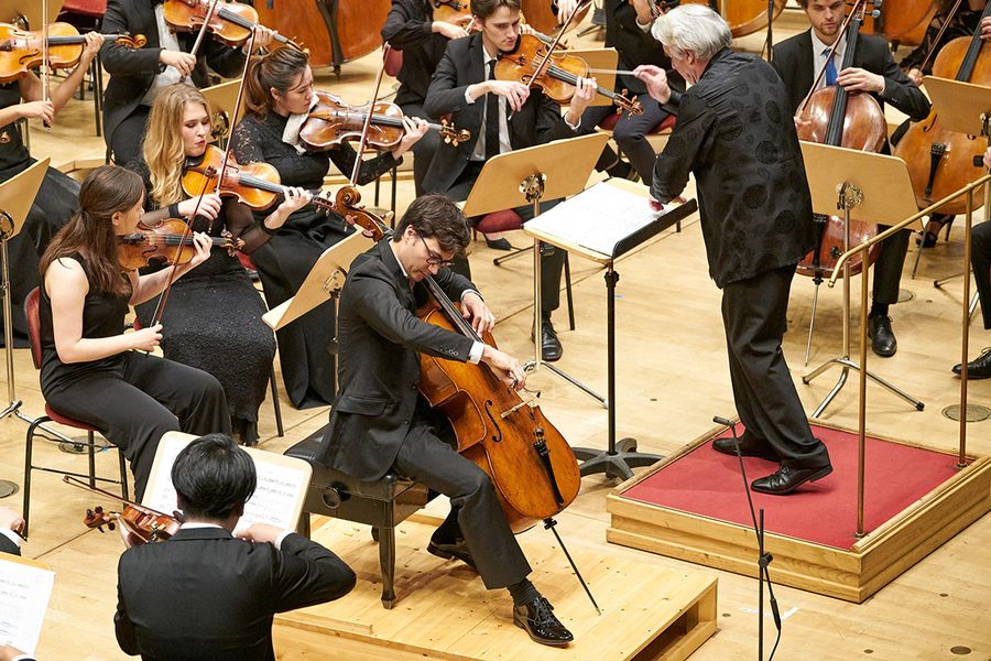 Cellosolist und Dirigent vor einem Orchester während eines Konzertes