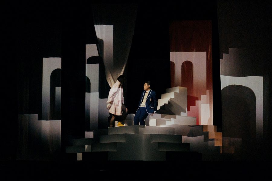 Zwei Gesangstudierende während einer Musiktheater-probe inmitten eines kontrastreich projizierten Bühnenbilds aus Treppen und Torbögen