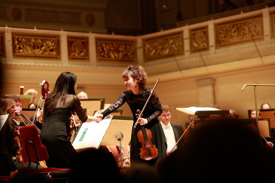 Geigensolistin reicht Konzertmeisterin auf der Bühne die Hand
