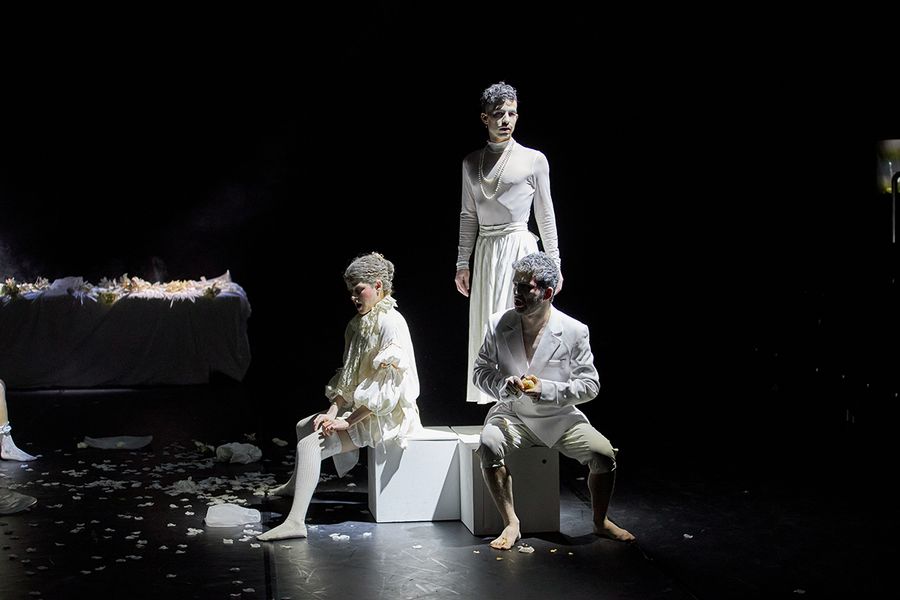 drei weiß gekleidete Darsteller auf einer dunklen Bühne