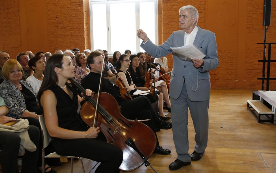 Eberhard Feltz steht vor einem Publikum und Studierenden mit Streichinstrumenten 