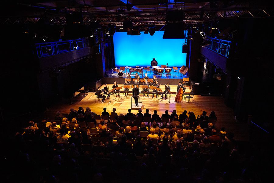 Dirigenten und Ensemble auf einer Bühne in einem Saal mit Publikum