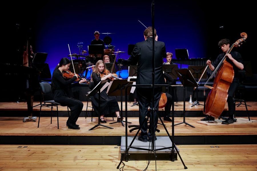 Dirigent dirigiert ein Streichensemble auf der Bühne des Studiosaals