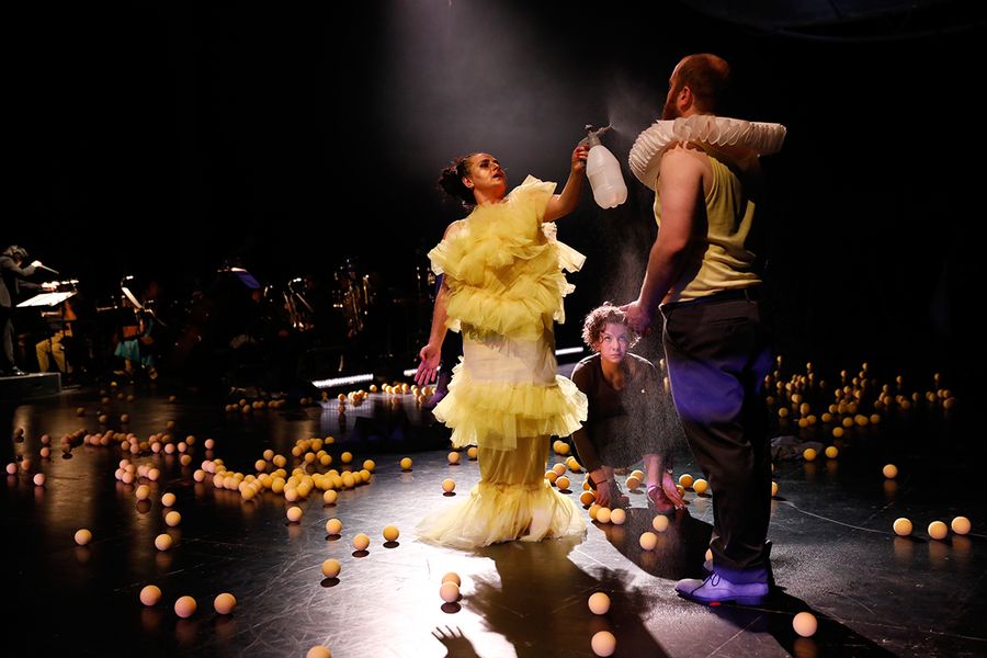 gelbe Bälle und zwei Personen in bunten Kostümen auf einer Opernbühne