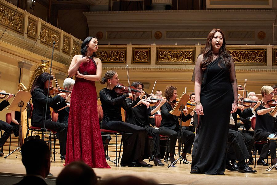 Zwei singende Studentinnen vor einem Orchester