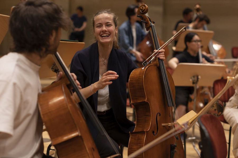 Studentin und Student halten ihr Cello in der Hand, Studentin lacht