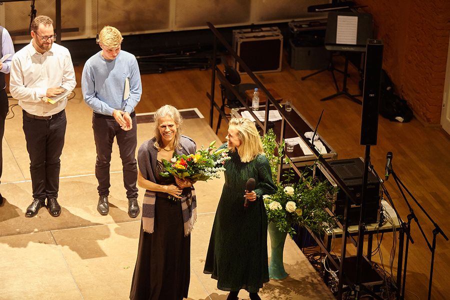 zwei Studenten, Rektorin und Organisatorin Claar Ter Horst mit Blumenstrauß auf einer Bühne