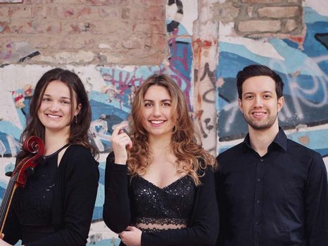 Zwei Musikerinnen und ein Musiker mit Instrumenten vor einer Graffiti-Wand