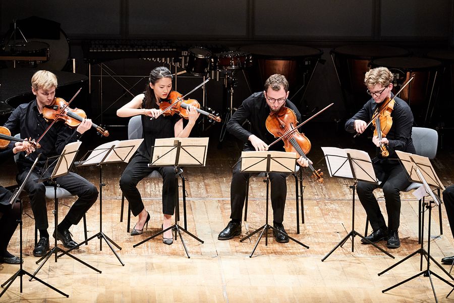 Vier Studierende mit Geigen und Bratschen sitzen auf einer Bühne