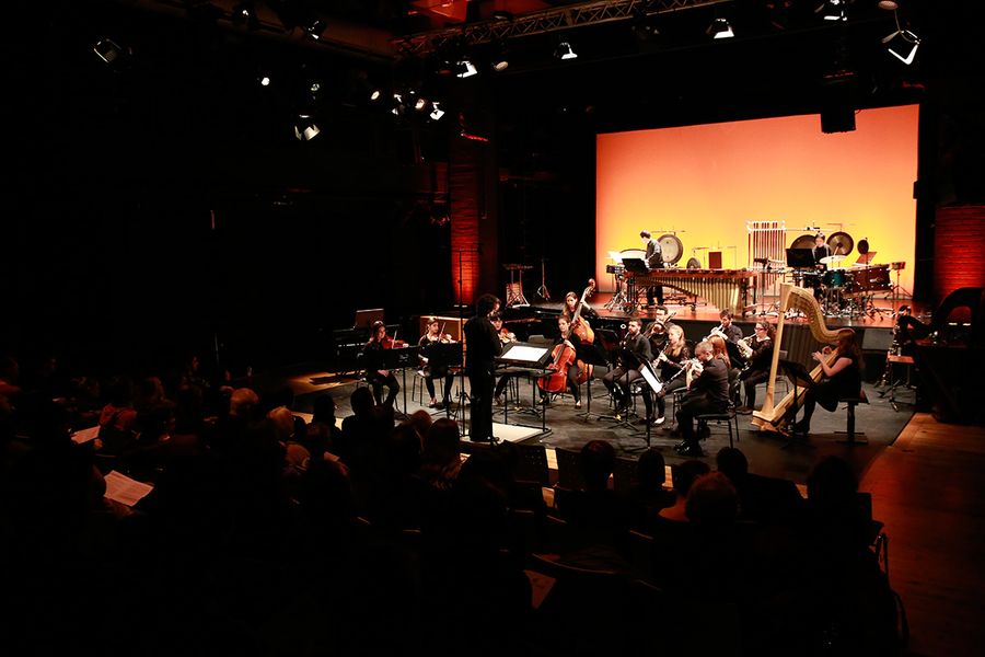 Ensemble mit Dirigent auf einer Bühne während eines Konzertes vor Publikum
