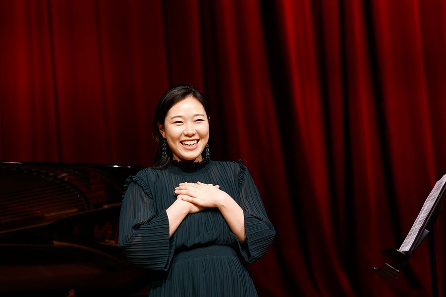 Lachende Gesangstudentin auf der Bühne des Studiosaals vor rotem Vorhang
