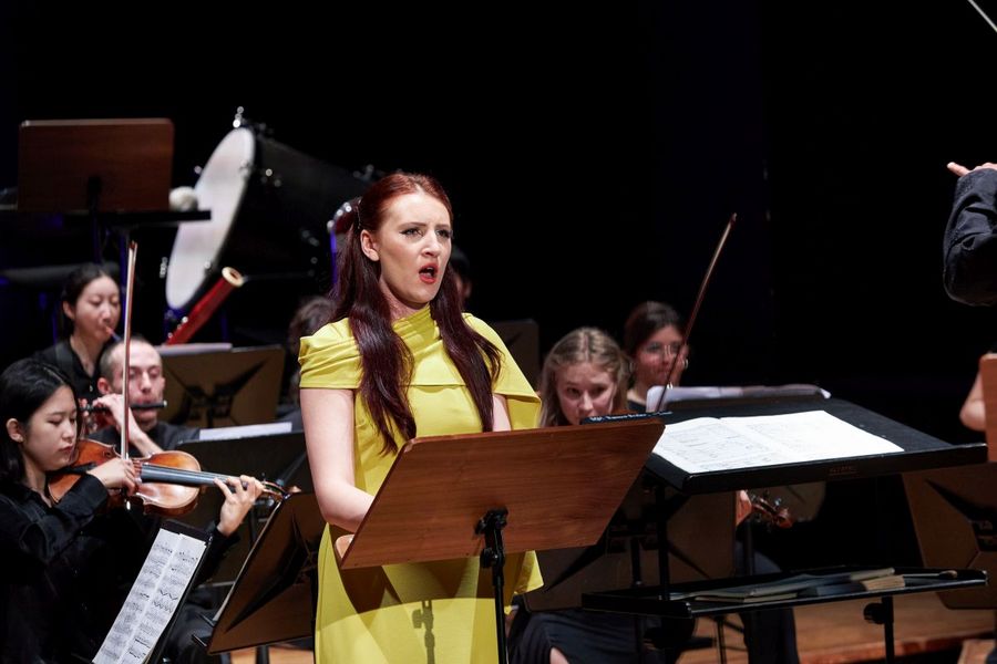 Eine Sängerin in einem gelben Kleid steht vor einem kleinen Ensemble und singt