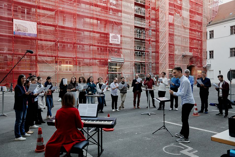 Hochschulangehörige stehen im Innenhof des Marstalls um einen Dirigenten und Keyboard und singen