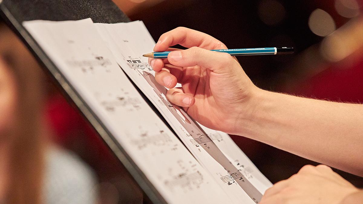 Hand schreibt etwas mit Bleistift auf ein Notenpapier