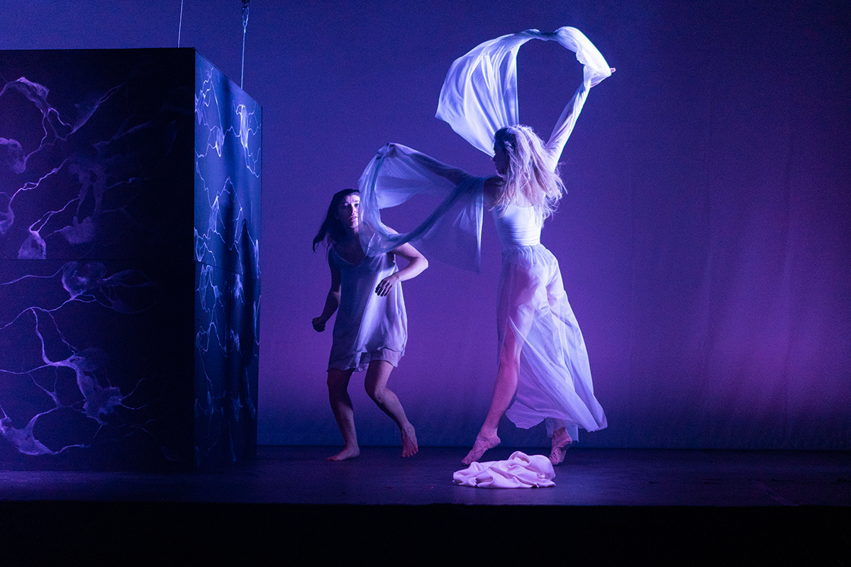 Gesangstudentin und Tänzerin mit weißen Tüchern auf einer blau beleuchteten Bühne