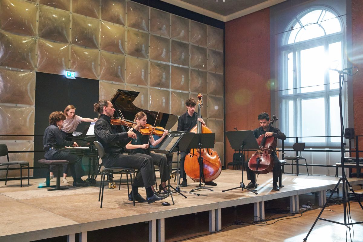  Vier Streicher und ein Pianist spielen auf der Bühne des Krönungskutschen-Saals, Studentin steht neben dem Pianisten zum Blättern