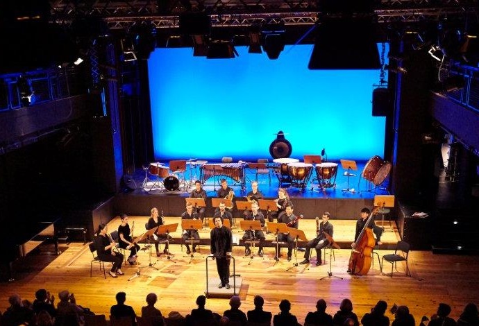 Kammerorchester mit Dirigent auf einer Bühne vor Publikum während eines Konzertes